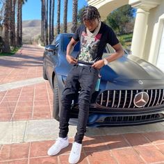 a young man sitting on the hood of a sports car looking at his cell phone