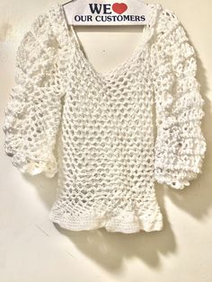 a white top with crocheted sleeves hanging on a wall next to a sign that says we love our customers