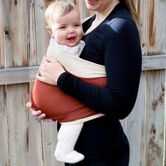 a woman holding a baby in a sling on her arm and smiling at the camera