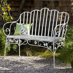 a white metal bench sitting in the middle of a gravel covered area next to a brick wall