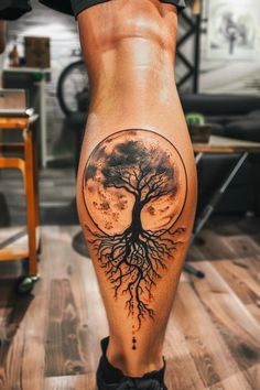 a woman's leg with a tree and moon tattoo on it