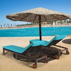 two chaise lounge chairs under an umbrella on the beach with blue water in the background