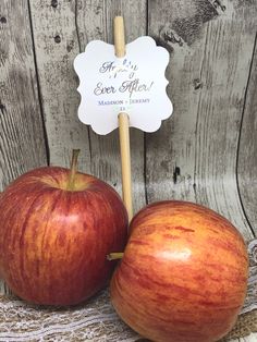 two apples sitting next to each other on top of a wooden table with a sign