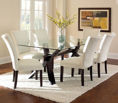 a glass dining table with white chairs and a rug on the floor in front of it