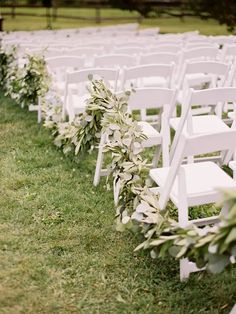 rows of white folding chairs lined up in the grass with greenery on each side