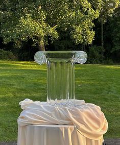 a glass vase sitting on top of a table covered in white cloth next to a tree