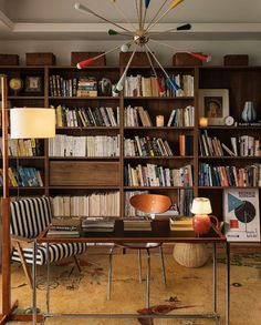 a living room filled with lots of books on top of a wooden shelf next to a lamp