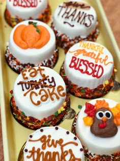 decorated cupcakes with thanksgiving sayings on them in a yellow tray, sitting on a wooden table