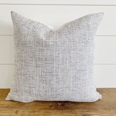 a gray pillow sitting on top of a wooden table next to a white brick wall