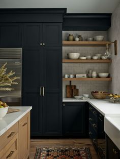 a kitchen with black cabinets, white counter tops and wooden shelves filled with dishes on top of them