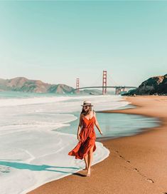 a woman walking along the beach in front of the golden gate bridge