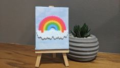 an easel with a rainbow painting on it next to a potted succulent