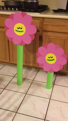 two pink flowers sitting on top of green poles in the middle of a kitchen floor