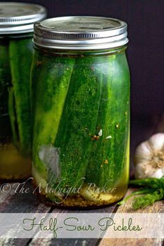 three jars filled with pickles sitting on top of a wooden table next to garlic