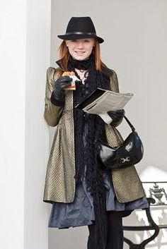 a woman in a hat and coat standing next to a wall with an open book