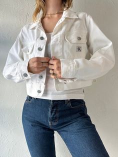 - Vintage Calvin Klein white cropped denim jacket - 100% cotton - Made in Canada - Tagged S Chest: 20" Length: 18.5" Sleeve: 23.5" We are not responsible for lost, stolen, or damaged packages once they have been shipped. Any additional customs duties or taxes incurred on international orders are the responsibility of the buyer. Please note that our items are vintage and may have minor flaws or imperfections due to their age, which adds to their unique character. Fitted Cotton Cropped Jacket For Streetwear, Fitted Cotton Cropped Jacket For Spring, Spring Fitted Cotton Cropped Jacket, Spring Streetwear Cropped Jacket, Cropped Cotton Outerwear For Streetwear, Cropped Jacket For Spring Streetwear, Spring Cropped Jacket For Streetwear, Spring Streetwear Cropped Jacket With Button Closure, Trendy White Cropped Denim Jacket