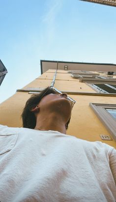 a man with his eyes closed looking up at something in the air above him and below him is a tall building