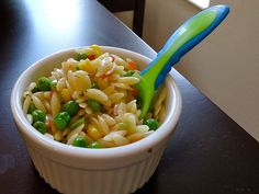 a white bowl filled with pasta and peas on top of a wooden table next to a window