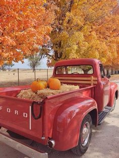 an old red truck with hay and pumpkins in the bed is parked by some trees