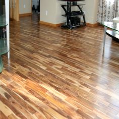 a living room with hard wood flooring and glass table in the center, looking into the dining room