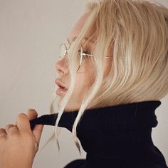 a blonde woman wearing glasses and a black turtle neck sweater is looking off to the side