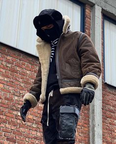 a man in a black mask and brown jacket is standing on a skateboard near a brick building