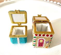 two small boxes sitting on top of a white table covered in beaded fabric and gold trim