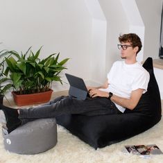 a young man sitting on a bean bag chair using his laptop computer while looking at the screen