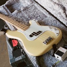 an electric bass guitar sitting on top of a bed next to a charger and power strip