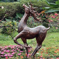 a statue of a deer is in the middle of some flowers and bushes with its head on it's hind legs