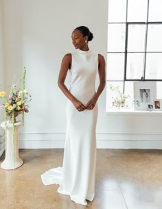 a woman standing in front of a window wearing a white dress and looking off to the side