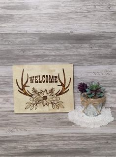 the welcome sign is next to a potted succulent plant on a white rug