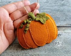 a hand holding a small felt pumpkin ornament with green leaves on the top