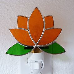 an orange and green flower is mounted on a white light switch cover with a single outlet