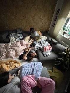 several people laying on top of a couch in a room with pillows and blankets around them