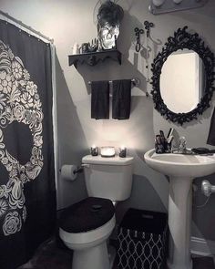 a black and white photo of a bathroom with skull decorations on the shower curtain, toilet seat cover, sink and mirror