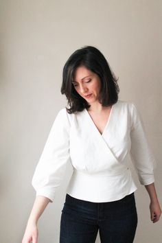 a woman standing in front of a white wall holding a piece of cake with one hand