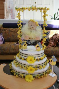 a three tiered cake decorated with yellow flowers and a teddy bear on the top