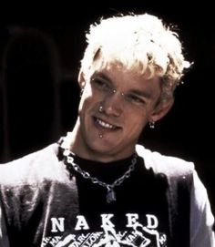 a young man with blonde hair wearing a black shirt and silver chain around his neck