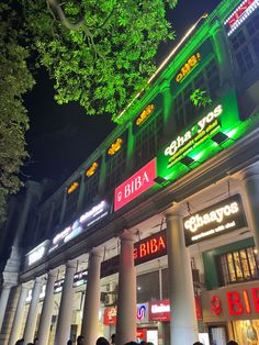 a group of people standing in front of a building with neon signs on it at night