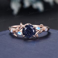 a blue diamond ring sitting on top of a black surface with leaves and stones around it