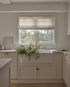 a kitchen with white cabinets and a window above the sink that has a gold faucet on it