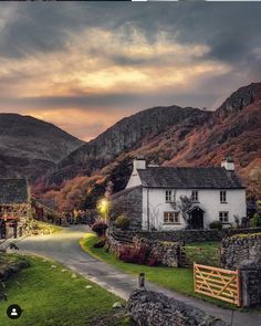 a house in the middle of a country road with mountains in the background at sunset