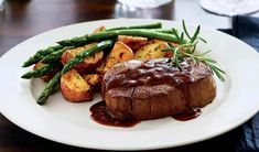 a white plate topped with steak and potatoes covered in gravy next to asparagus