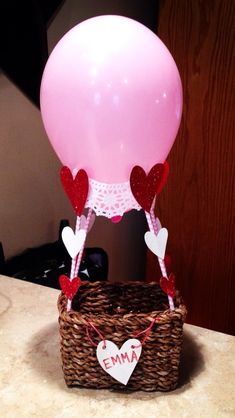 a pink balloon with hearts attached to it in a wicker basket on a table