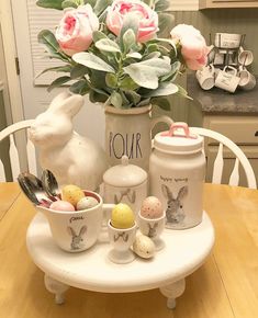 a table topped with eggs and flowers on top of a wooden table next to a vase filled with pink roses