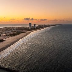 an aerial view of the beach and ocean at sunset with buildings in the back ground