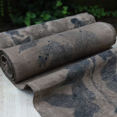 two rolls of fabric sitting on top of a white cloth covered in black ink with trees in the background