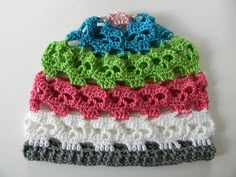 four crocheted hats are stacked on top of each other, all in different colors