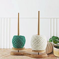 two balls of yarn sitting on top of a wooden stand next to a potted plant